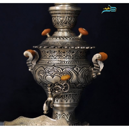 نمای نزدیک سماور برنجی قلمزنی امضادار و جزئیات ظریف نقش‌های دست‌ساز روی بدنه.
